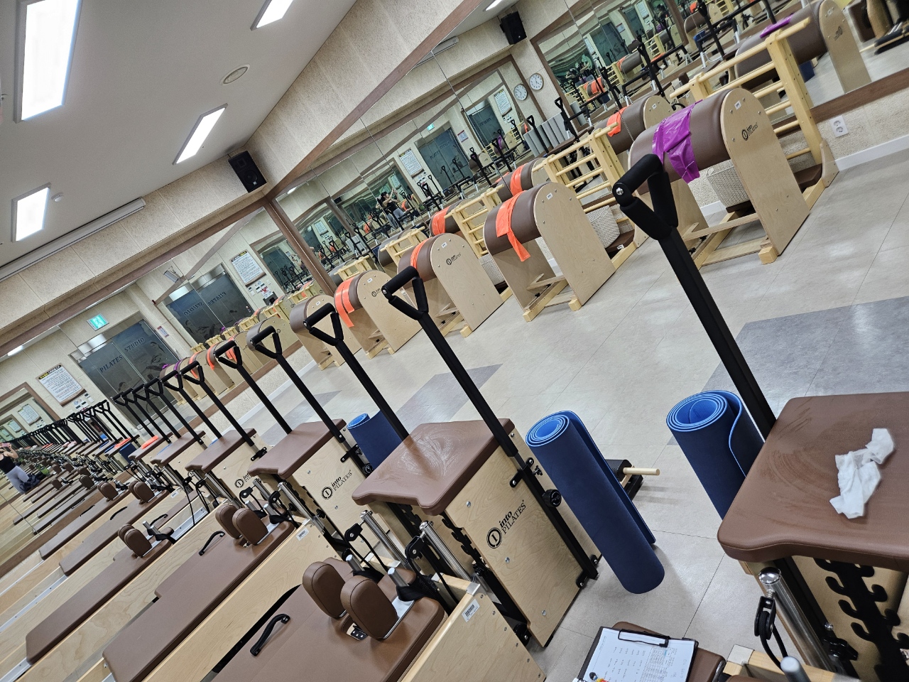 필라테스 스튜디오 내부 사진이며, 안쪽 벽면 거울 앞에 바렐이 있고 좌측에는 리포머와 체어 등 기구 필라테스를 위한 기구가 위치해 있습니다.