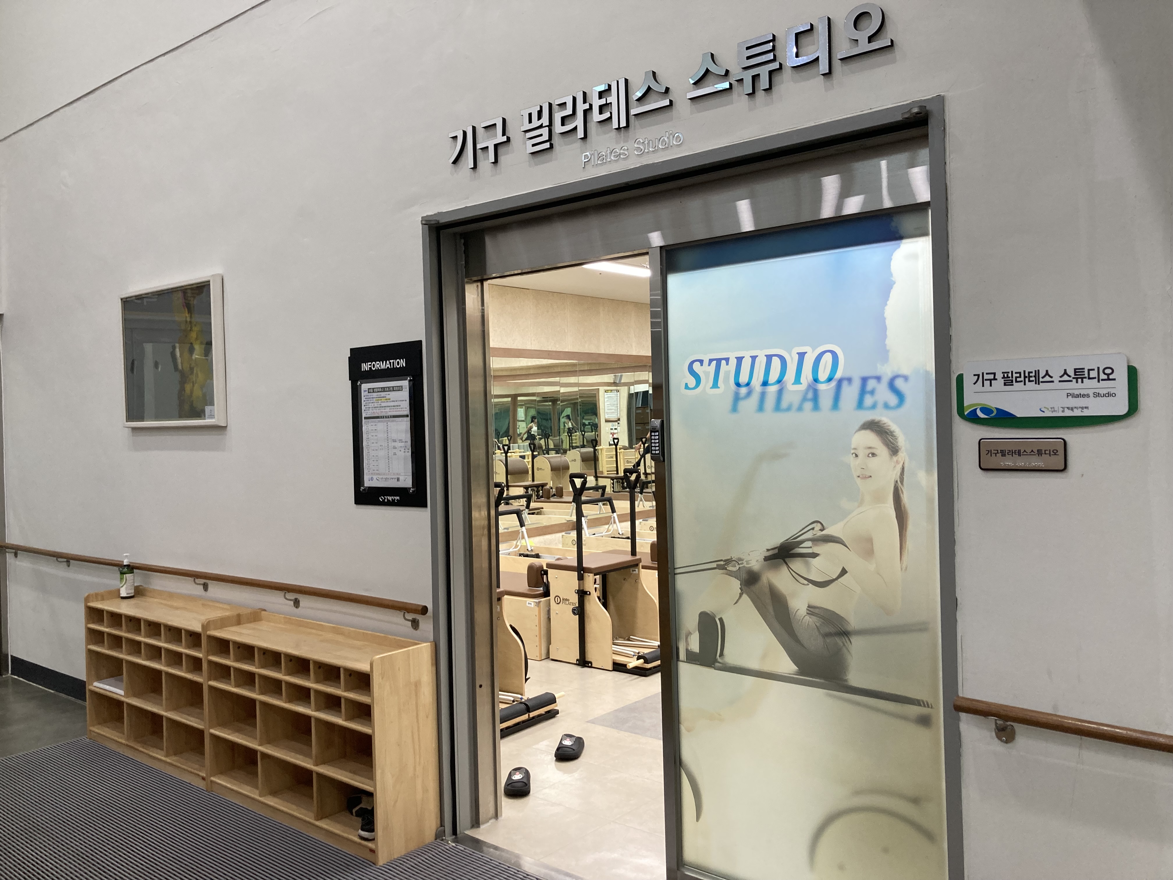 기구 필라테스 스튜디오 입구 사진이며, 좌측에는 프로그램 안내를 위한 안내판과 그 아래는 신발을 두는 신발장이 위치해 있습니다.